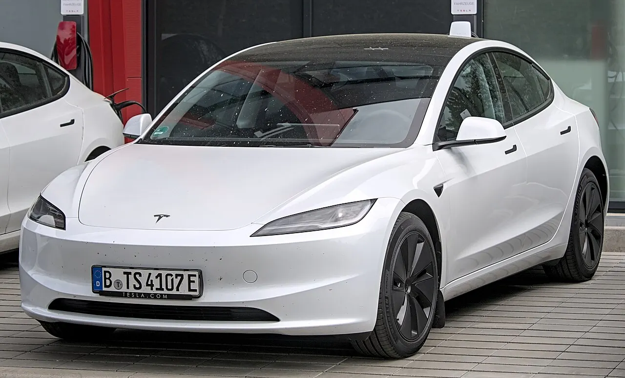 Vit Tesla Model 3 av den uppdaterade generationen parkerad utanför en Tesla-anläggning