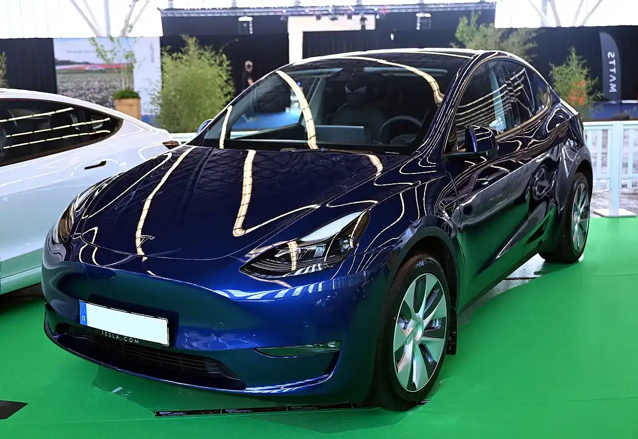 Blå Tesla Model Y fotograferad snett framifrån i en utställningshall