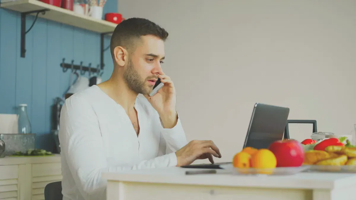 Person som talar i telefon framför en laptop i ett kök